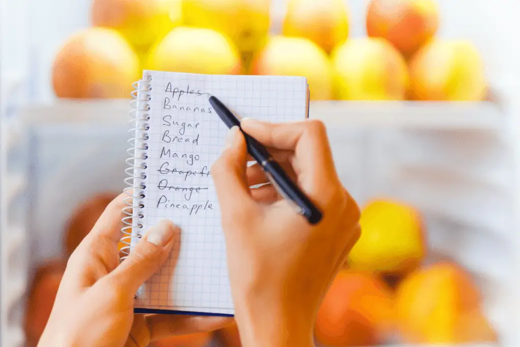 A woman's hands holding a pad and pen and crossing off a grocery shopping list